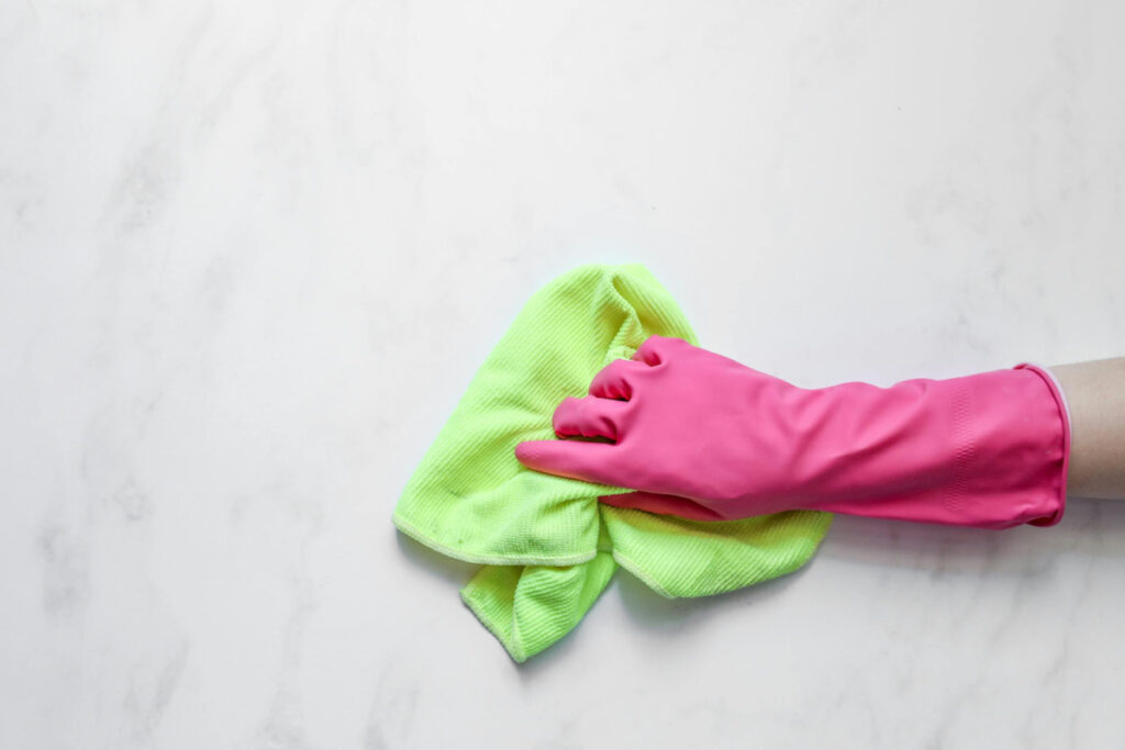 Hand in pink glove holding a green microfiber towel.