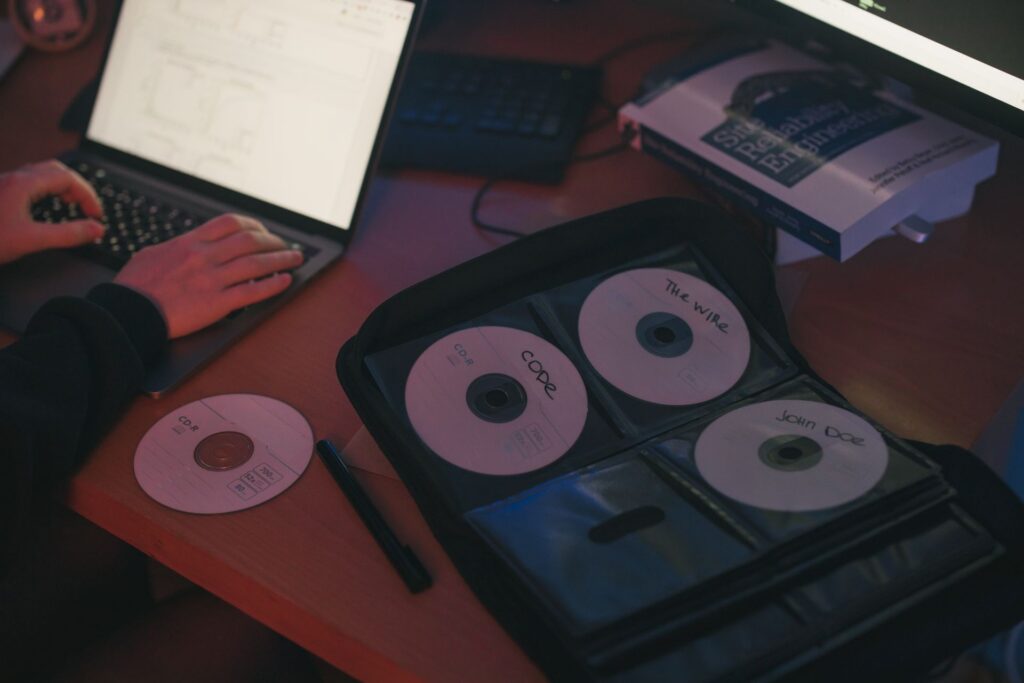 A person using a laptop with a CD binder next to them